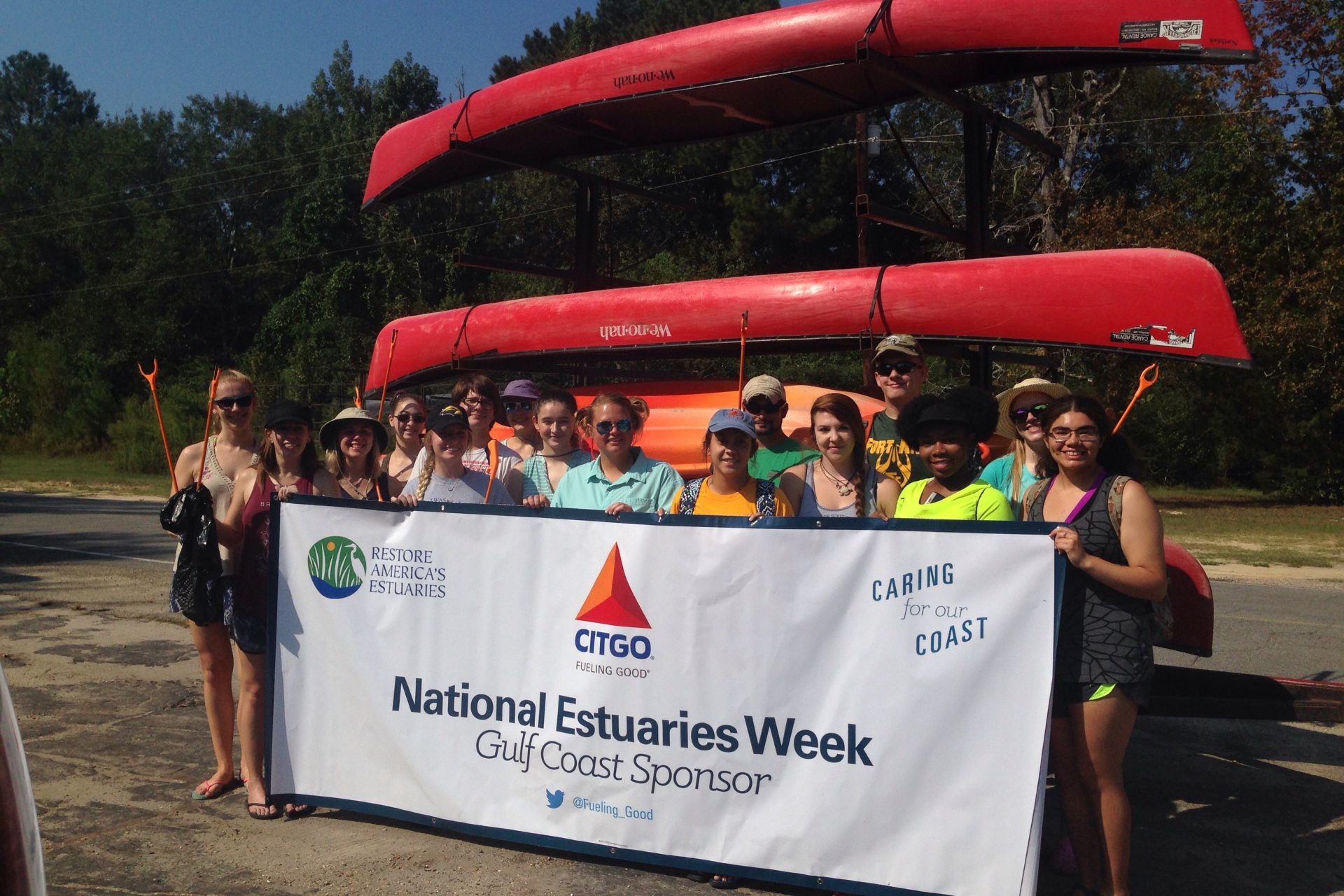 Group of 16 young people standing in front of canoes holding a banner that says National Estuaries Week